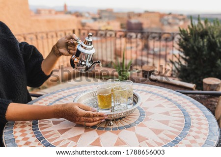 Woman hand pouring traditional moroccan mint tea in glasses. Vintage silver tray and teapot. Round mosaic table. Morocco hospitality.