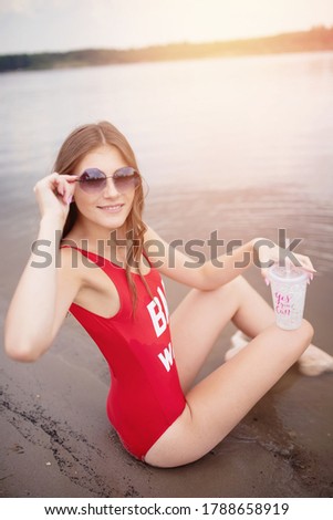 Young woman in red swimsuit holds glass with cocktail on beach.