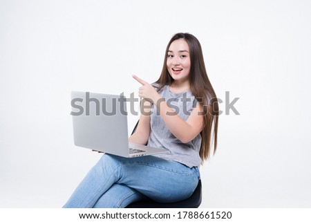 Portrait of casual asian woman holding laptop computer while sitting on a chair over white background