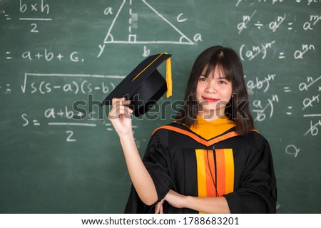Asian female graduates wear a black robe and black hat with golden tassels. Standing in front of the blackboard in the classroom