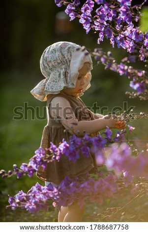 Cute funny little girl in panama hat is looking at beautiful blue flowers. Image with selective focus and toning