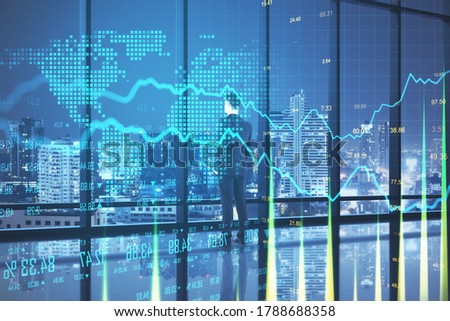 Thoughtful businessman standing in abstract office interior with glowing forex chart and night city view. Hologram and finance concept. Double exposure