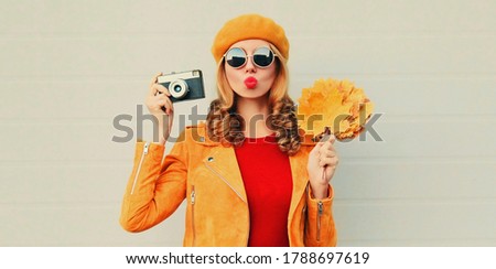 Autumn portrait of attractive woman with retro camera and yellow maple leaves wearing french beret over gray background