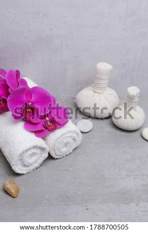 Concept for spa salon, rolled  towel and branch red orchid.,with herbal ball,stone on gray background, Copy space
