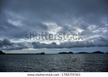 Seascape during the dark rain clouds cover island and harbor at the sea coast in Panwa cape, Phuket Island. Dark storm clouds made overcast ambience. Natural disaster by rainstorm. Nimbostratus cloud. Royalty-Free Stock Photo #1788709361