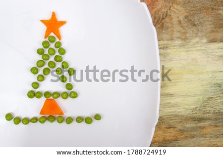 Creative photo of green peas and carrots in the form of a Christmas tree on a white plate, copy space, background, top view, close up. Concept of food art, Breakfast for children, new year holiday