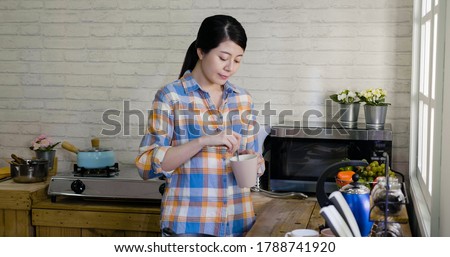Young asian korean female stir cup of coffee in morning at home kitchen. elegant girl smiling preparing drink for breakfast. relax lady mixing sugar into mug while standing against window indoors Royalty-Free Stock Photo #1788741920