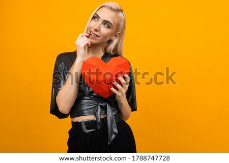 European attractive girl hugs a 3D heart figure on an orange studio background. Valentine's Day