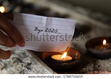Hand holding a white note paper written - Bye 2020. Burning it on a burning candle in a ceramic bowl. Hope, new life and new year 2021 concept. Royalty-Free Stock Photo #1788750659