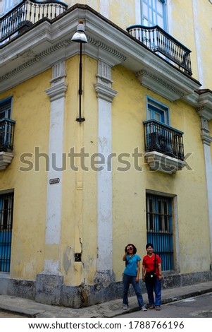 Two Asian female tourists standing at a corder of a colonial style building, taking a picture, in old town Havana, Cuba.