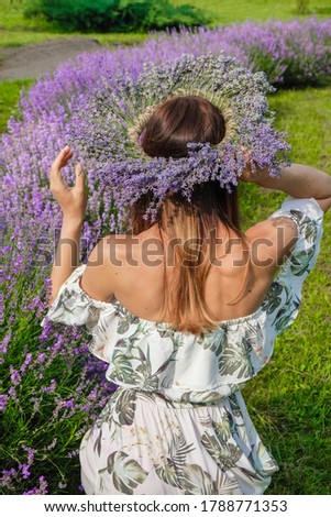 Young woman with bare shoulders on a lavender background. The woman has a lavender wreath on her head. Vertical image.