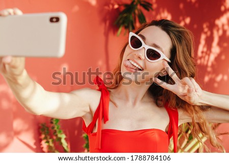 Happy beautiful woman in bikini and sunglasses making selfie photo on smartphone outdoors