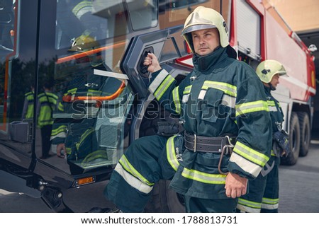 Waist up portrait of handsome young man open door of modern fire truck