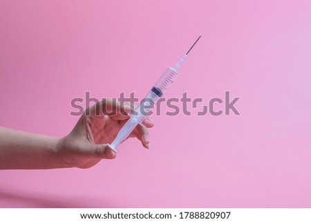Hand holding syringe on pink background