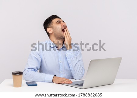 Bored exhausted man employee sitting office workplace with laptop on desk, yawning covering face with hand, feeling fatigued of overtime work, night shift. studio shot isolated on white background