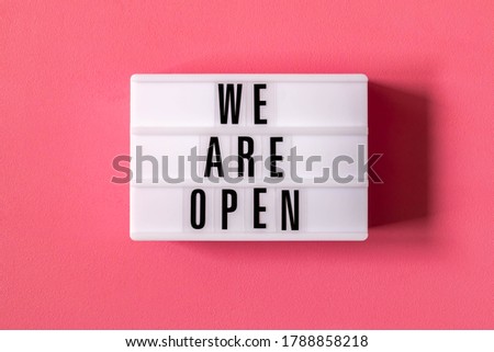 Signboard WE ARE OPEN of lightbox on red background. Open sign hanging on blue wall. Business open and welcome. Opening sign of cafe, bar, or restaurant. Concept of quarantine mitigation