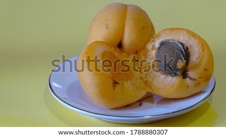 Two ripe apricots on a platter on a yellow isolate. One apricot cutaway. Expressive position. Summer. Food. Background picture.