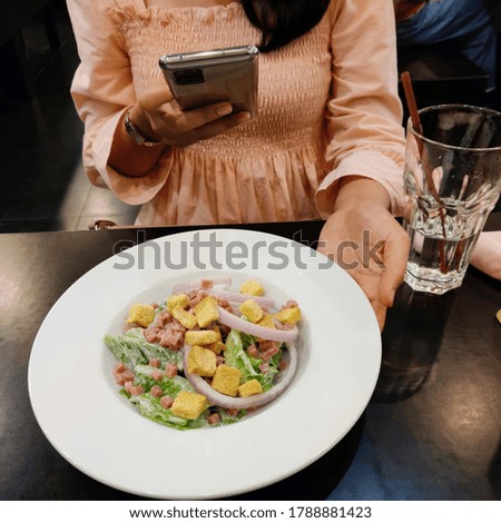 Asian woman using smartphone to taking photo of salad in a white plate on table in cafe, communication in social networks