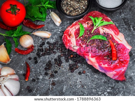 The picture of fresh raw rib eye steak of beef on stone dish with salt, pepper,garlic,tomato,and
 basil garnish in a simple style.