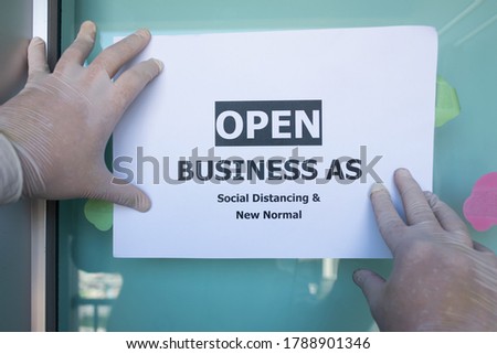 Placing open sign “OPEN BUSINESS AS SOCIAL DISTANCING & NEW NORMAL” on front door. Reopening for business adapt to new normal in the Coronavirus COVID-19 pandemic. Office Opening,