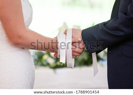 Wedding ceremony moment, bride and groom's hands tied with white ribbons, white wedding dress, dark suit Royalty-Free Stock Photo #1788901454