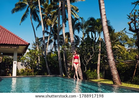 Young woman in red swimsuit standing neat the beautiful swiming pool