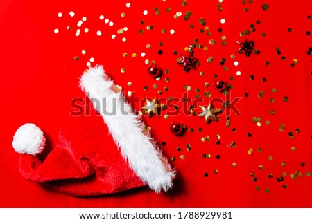 Santa Claus hat on a red background, gold sequins and Christmas toys, mock up