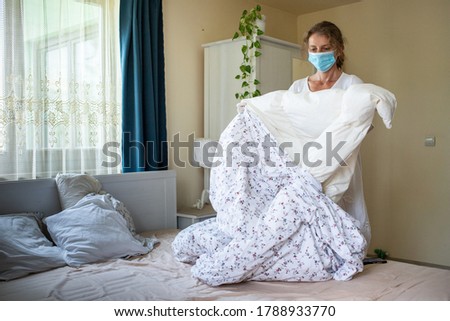 woman changing bed sheets wearing medical mask - hotel industry during pandemic