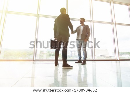 Two businessmen handshake in office with big panoramic windows