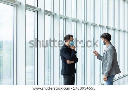 Two employee standing in social distance wearing face mask looking at each other and talking in the office. Royalty-Free Stock Photo #1788934655