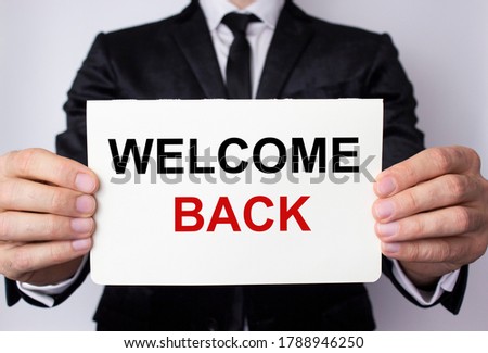 Welcome back inscription on a white sheet of paper in the hands of a businessman on a white background. The concept of returning to the office, school, work, university.