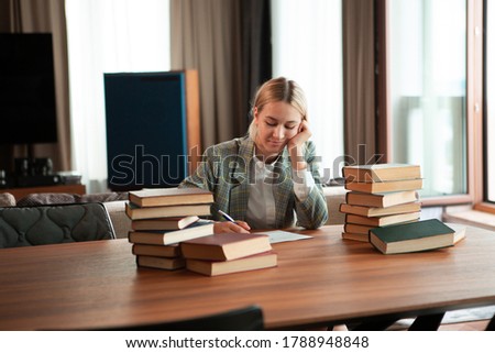 Young cute smiling girl student sitting with books at table in classroom or library. Back to school