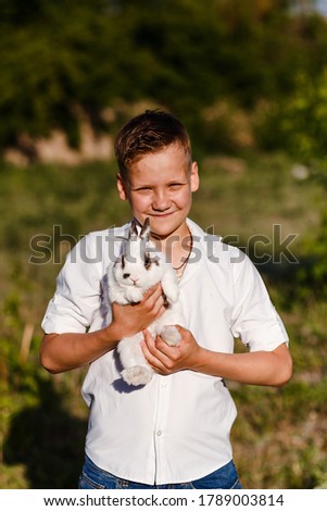 Smiling ten-year-old boy holds a little white rabbit outdoors