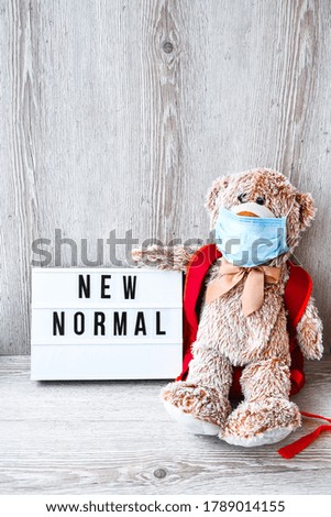 Coronavirus covid-19. Teddy bear doll wearing mask backpack and holding lightbox with text NEW NORMAL on wooden background, copy space, Quarantine 2020. Back to school