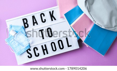 Lightbox with text BACK TO SCHOOL protective face mask and sanitizer. New normal. Books falling from backpack. Social distancing. Education in quarantine 2020