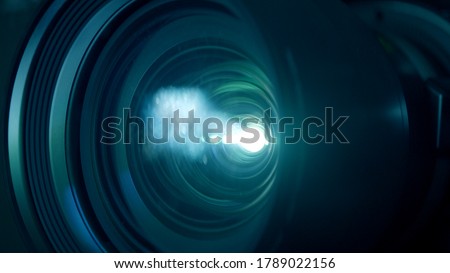 Macro closeup locked shot with selective focus of activated film projector. Illuminated lens and white light flare in dark room. Royalty-Free Stock Photo #1789022156