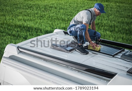 Caucasian Men in His 40s Cleaning Camper Van RV Roof Installed Solar Panels Using Sponge and Soft Washing Detergent. Motorhome Maintenance. RV Industry Theme.