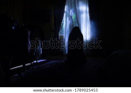 Horror silhouette in window with curtain inside bedroom at night. Horror scene. Halloween concept. Blurred silhouette of ghost