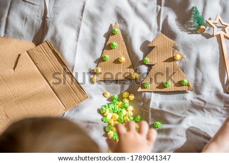 A child carves a Christmas tree from cardboard. Christmas decoration, hand made and Zero waste. child makes crafts on the bed at home. Div. Flat lay, top view.