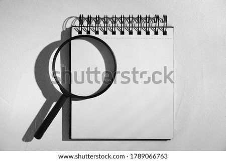 Magnifier glass and empty notebook on light stone background, flat lay with space for text. Find keywords concept