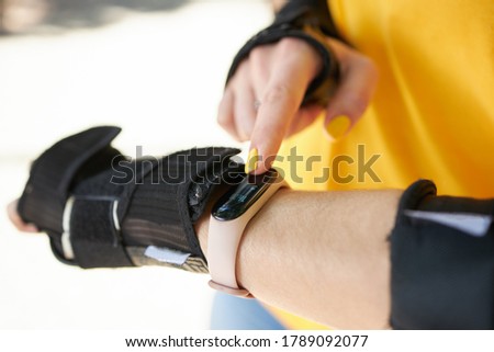 female person touching smart watch or fitness tracker while roller skating leisure activity. close up. sunny day. girl wearing hand protection for sport exercises.
