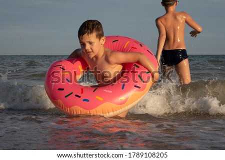 A 5-year-old boy swims in the sea with a donut-shaped inflatable circle with his older brother 10 years old. Two brothers indulge in the water