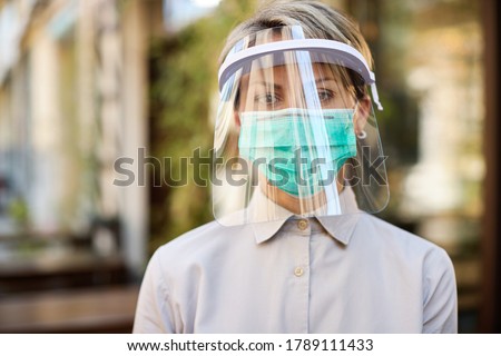 Portrait of waitress wearing visor and protective face mask while working at cafe during virus epidemic. Royalty-Free Stock Photo #1789111433
