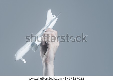 Miniature airplane in hand on a gray depressing background. The concept of the risk of a crash, the insurance of flights.