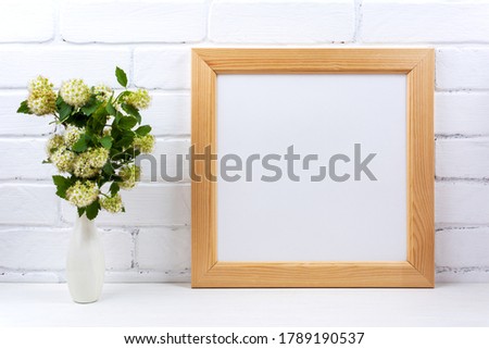Wooden square picture frame mockup with white spirea branch in the vase. Empty frame mock up for presentation design. Template framing for modern art.