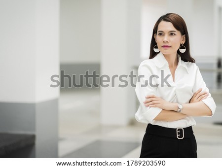 Portrait of a cheerful middle-age businesswoman in business suit standing in the company building with confidence arms crossed. Business stock photo.
