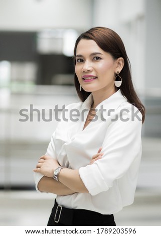 Portrait of a cheerful middle-age businesswoman in business suit standing in the company building with confidence arms crossed. Business stock photo.