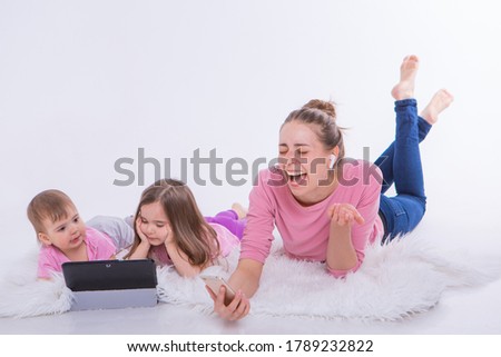 Modern technologies in everyday life: woman talks on phone through headset, children watch cartoon on tablet. Hobbies and recreation with gadgets. Family vacation. Parents with girls on floor