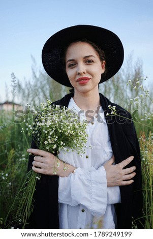      
portrait of a beautiful young woman in a hat enjoying the calmness and silence in a field with daisies                         
