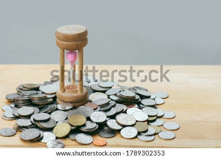 The hourglass is in the middle of a pile of silver coins piled on a wooden floor. The picture shows the concept of money that is about to run out.